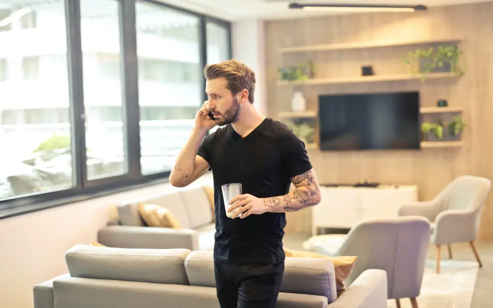 Man in a black T-shirt talking on his smartphone in a bright modern apartment