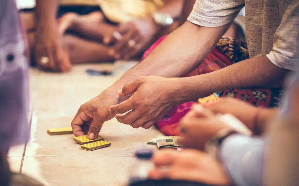 Friends gathered around a table game on the floor, hands reaching toward the pieces