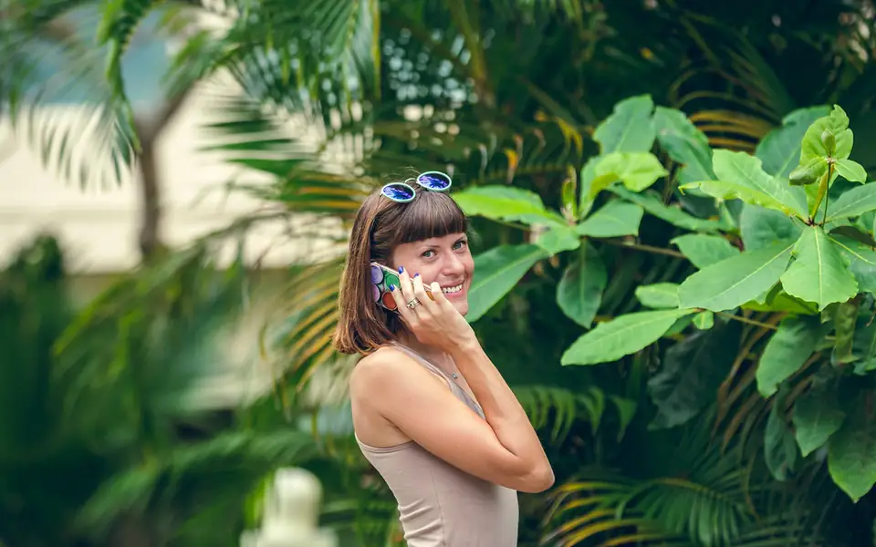 Young woman smiling while using her smartphone outdoors among tropical plants