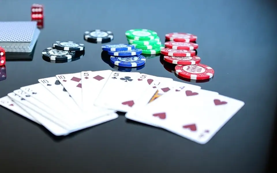 Poker chips, red dice and a spread of playing cards on a dark reflective table