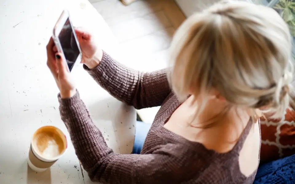 Woman with coffee checking her phone at a wooden table